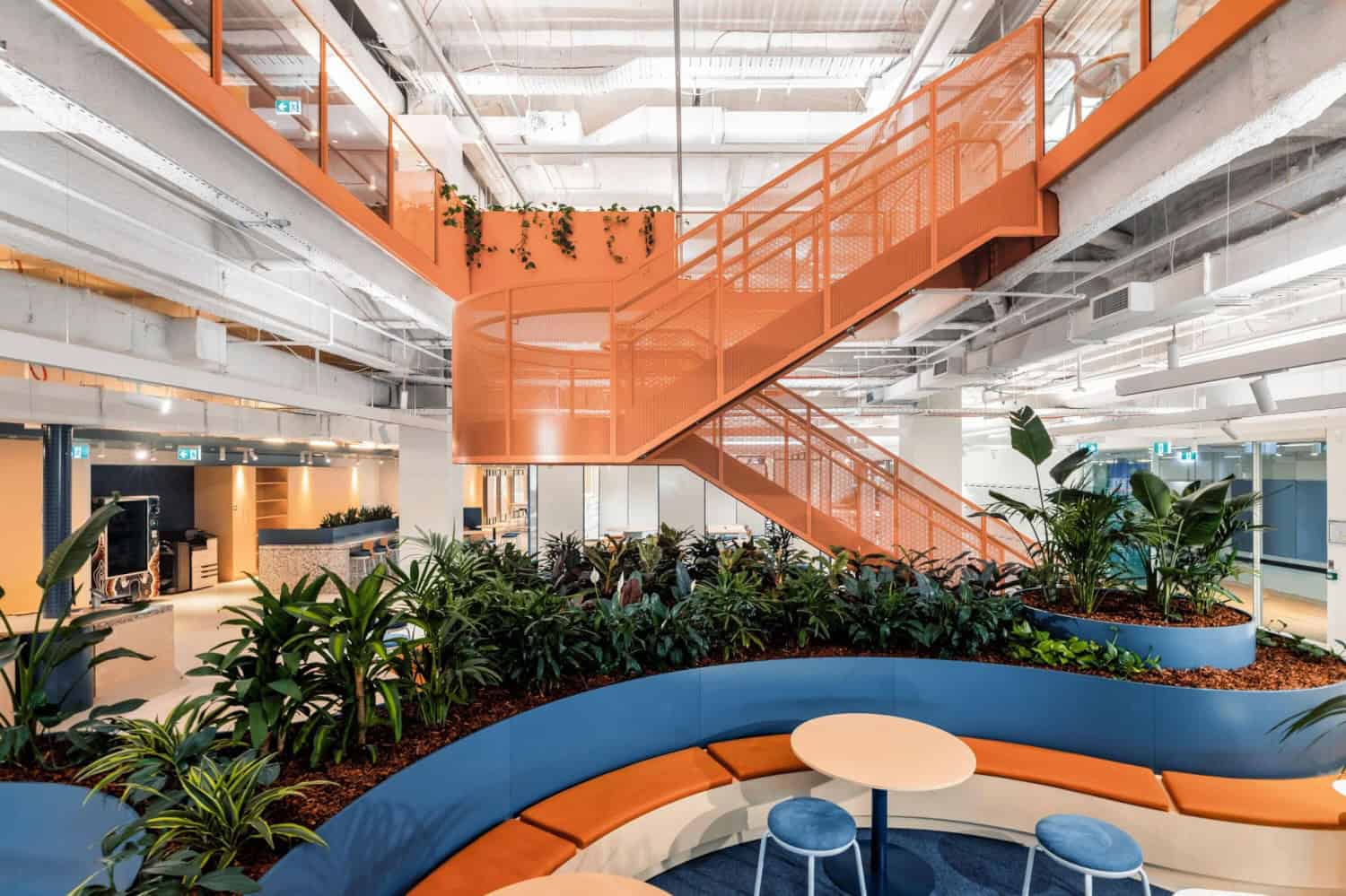 Orange staircase and curved seating areas in a corporate communal space full of indoor plants